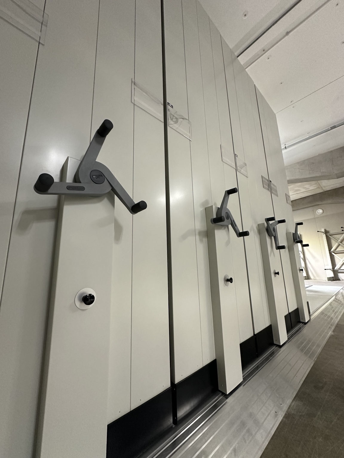 Row of mobile shelving units with hand wheels and floor tracks